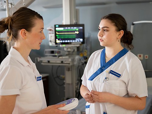 Två sjuksköterskor i samtal framför en monitor.