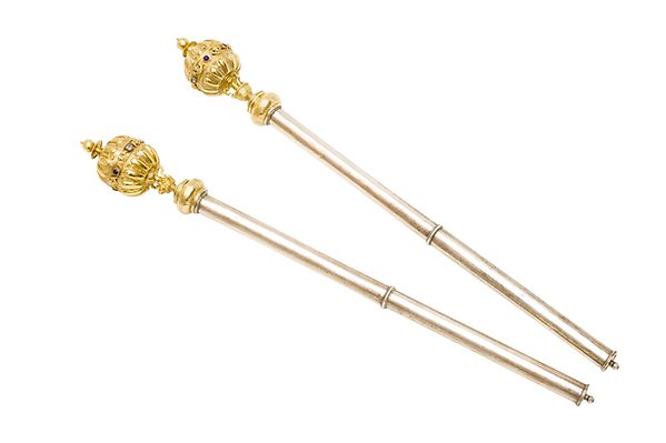 Two silver sceptres lie next to each other. Their tops are gilded, round and decorated with details and gemstones.