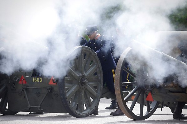 Smoke billows before men dressed in old-fashioned military uniforms and cannons that have just been fired. 