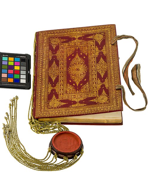 An old book with a colourful cover with many ornate details. A seal hangs from it, attached by golden strings. A paint palette lies beside the book.