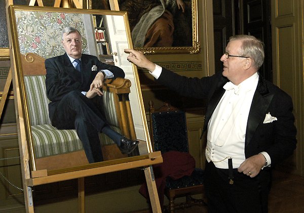 Stig Strömholm i högtidskläder pekar på målat porträtt på honom själv.