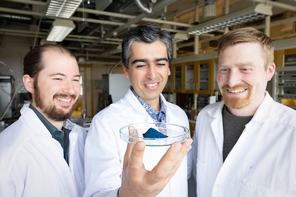 De tre forskarna i bild, en håller i en liten glasskål där det blåa pulvret ligger på en hög.
