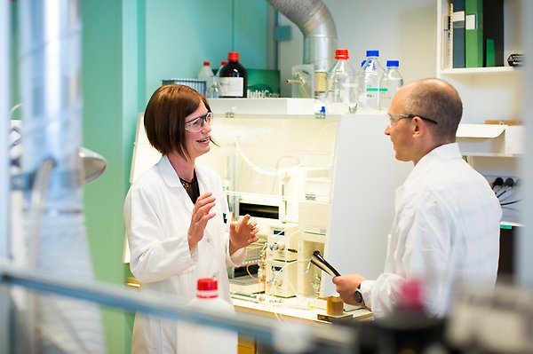 Två personer i labrock och skyddsglasögon på laboratorium