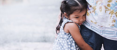 Ett litet barn kramar sin förälders ben. 